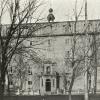 Photographie en noir et blanc représentant un édifice de cinq étages, avec un toit mansardé et un clocheton.